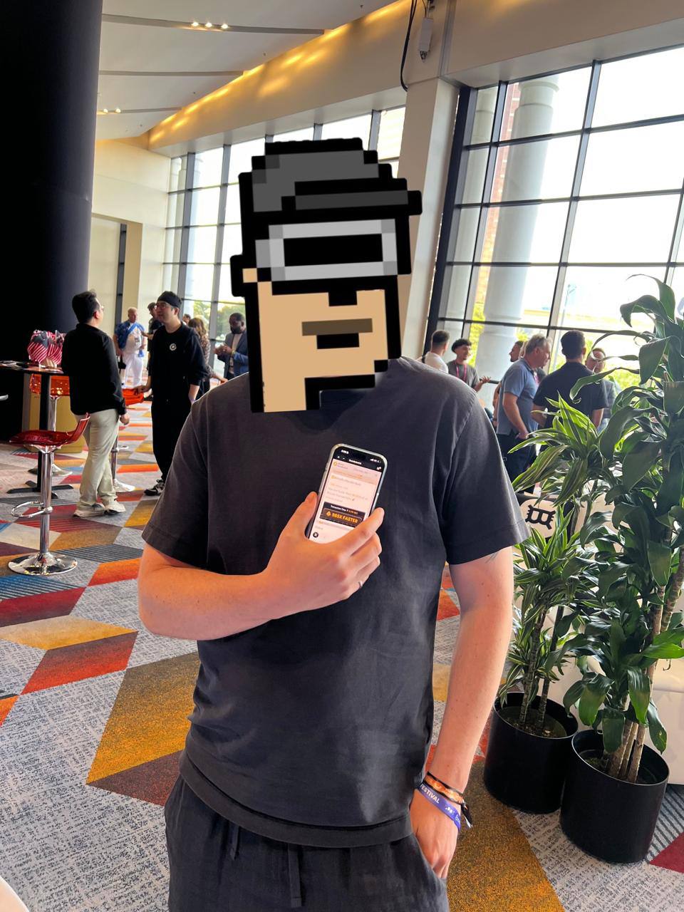 A Bitcoin 2025 attendee holding a phone displaying a Thunderbolt payment, with a pixel-art face covering preserved from the original photograph.