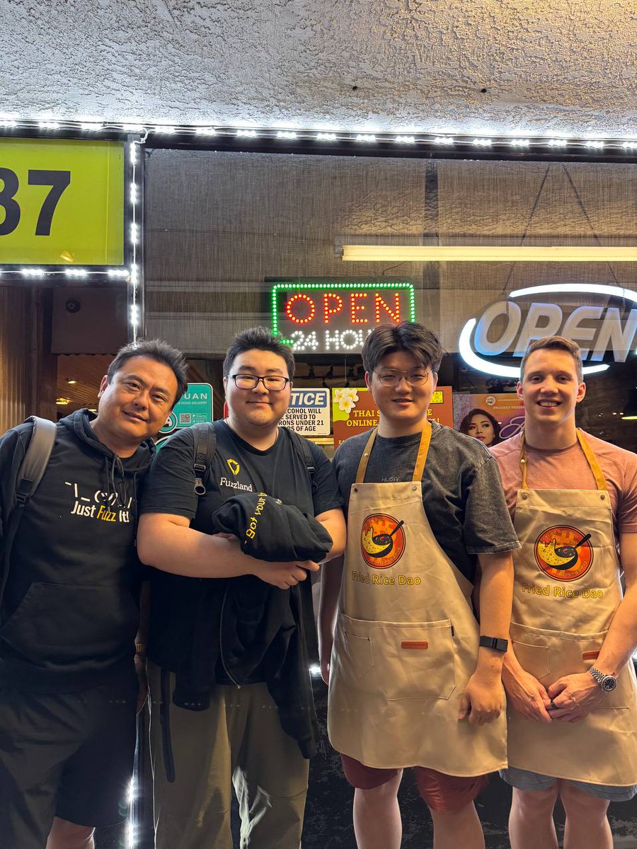 Four people outside a restaurant, two wearing Fried Rice DAO aprons.