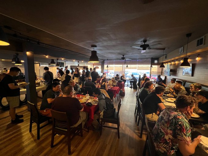 Guests eating and talking around closely packed tables inside the restaurant.